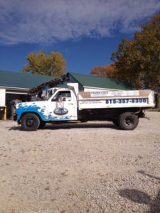 A Prairie State Water truck parked in front on a building on gravel near trees