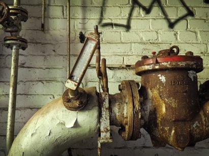 Old pumps and pipes with an attached meter in need of water well repair in front of a brick wall with graffiti