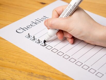 A hand holding a marker making check marks on a paper checklist on a wooden table.