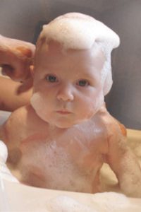 A baby in a bubble bath with an adults hands washing and holding it.